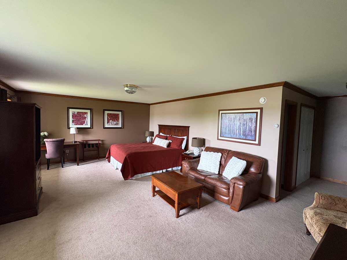 Large hotel suite with king bed, leather loveseat, armchair, coffee table, dresser, and spacious sitting area.