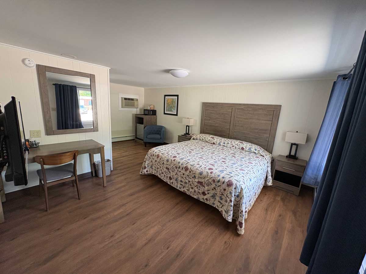 Renovated king room featuring luxury vinyl flooring, king bed, work desk, mini fridge, microwave, and seating area. 