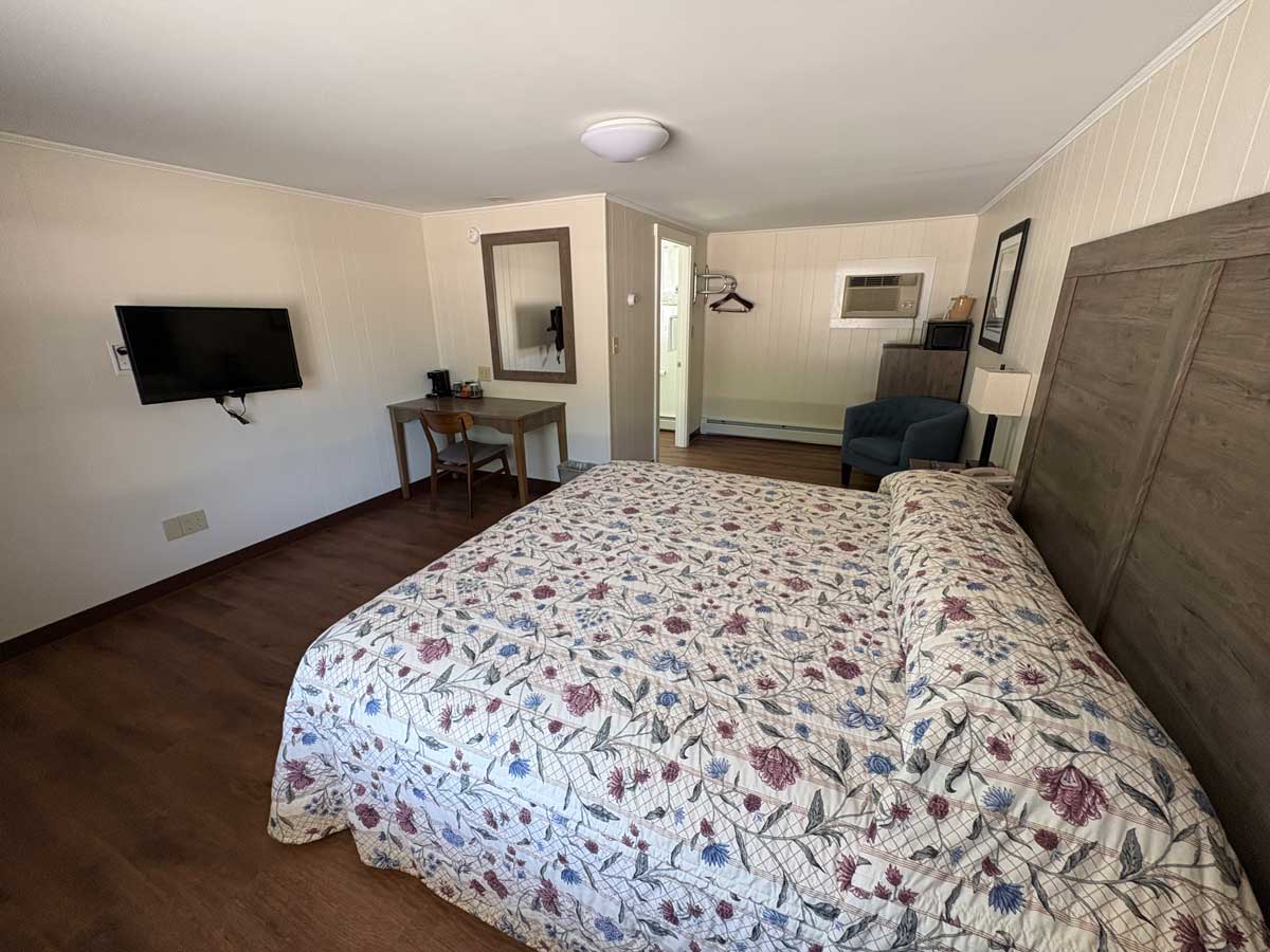 Spacious renovated king guest room with modern furnishings, king bed, wall-mounted TV, desk, mini fridge, and armchair.