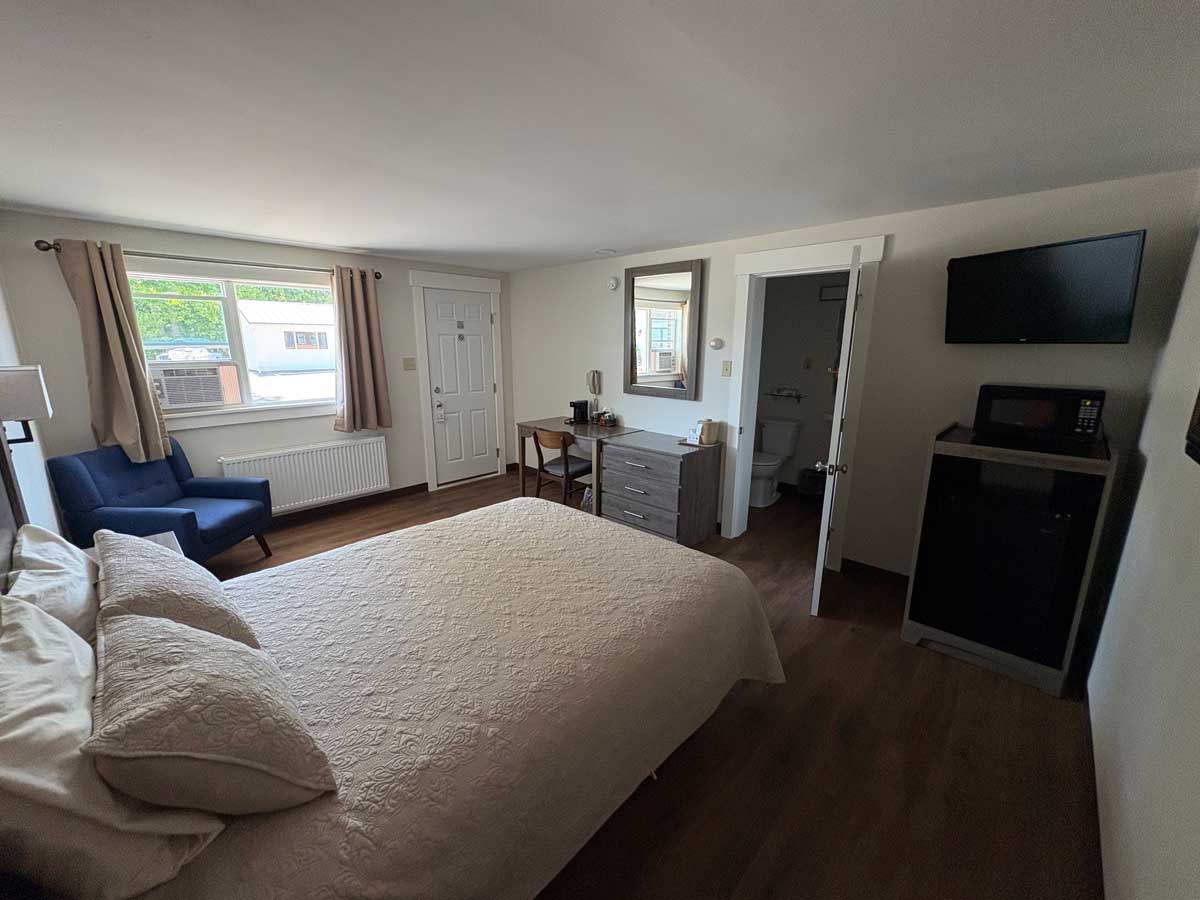 Modern renovated queen guest room featuring queen bed, work desk, mini fridge, microwave, and updated furnishings.